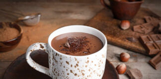 A cup of hot chocolate topped with chocolate shavings and surrounded by hazelnuts