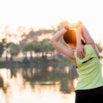 Revolutionary Study Shakes Up Back Pain Treatment A woman stretching her arms by a lake during sunrise