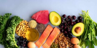 An assortment of healthy foods including fish, nuts, fruits, and vegetables arranged on a light background