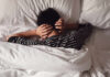 Child lying in bed with hands over ears