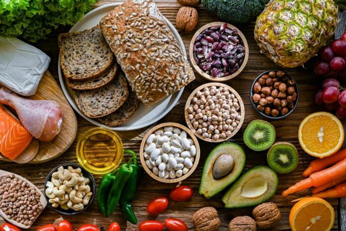 shutterstock_2483555019.jpg A variety of fresh foods including vegetables, fruits, grains, and proteins arranged on a wooden surface