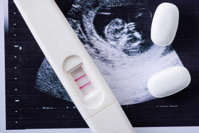 shutterstock_1506812507.jpg Pregnancy test next to an ultrasound image and two white tablets