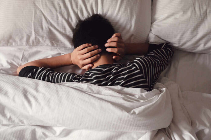 Preteen,Tween,Boy,Covering,Ears,With,His,Hands,In,Bed, Child lying in bed with hands over ears