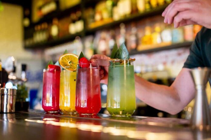 Row,Of,Vibrant,Cocktails,On,A,Bar,Counter,With,A A bartender preparing colorful cocktails at a bar