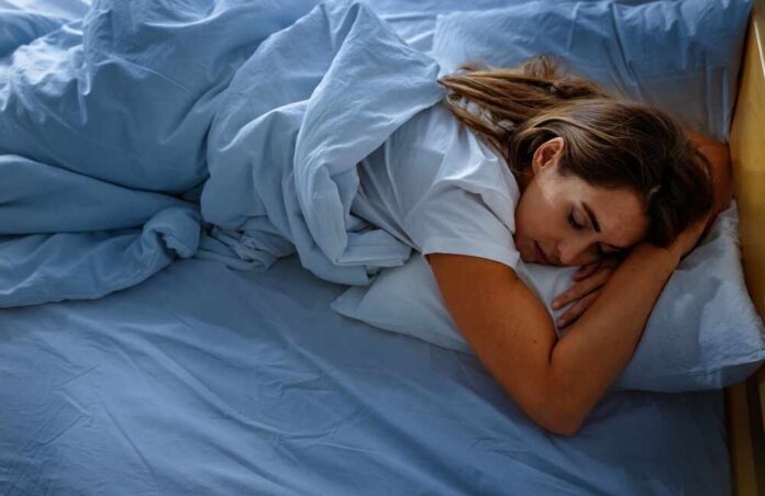 shutterstock_2711270941.jpg A woman sleeping peacefully on a bed with blue sheets