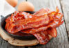 Crispy bacon strips in a cast iron skillet with eggs in the background