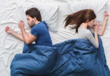 Couple sleeping back to back in bed under blue blanket