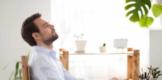 Man relaxing at desk with eyes closed beside laptop