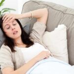 Woman resting on couch with hand on forehead