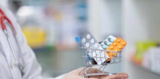 A doctor holding a miniature shopping cart filled with various medication packs
