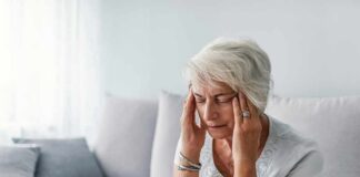 Older woman sitting on a couch holding her temples