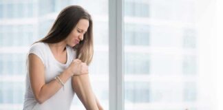 Woman sitting on yoga mat holding her lower leg in pain