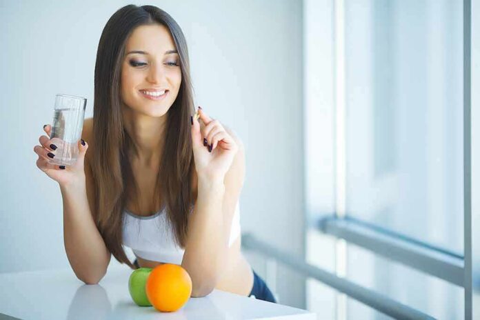 Woman holding a glass of water and a pill near citrus fruits
