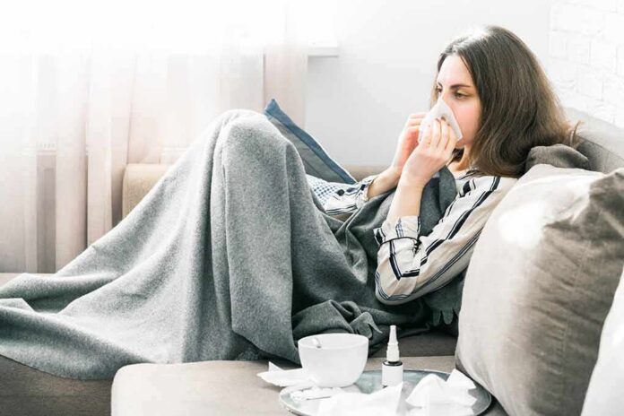 woman on couch blowing her nose under a gray blanket
