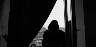 hooded figure sitting on a windowsill looking outside
