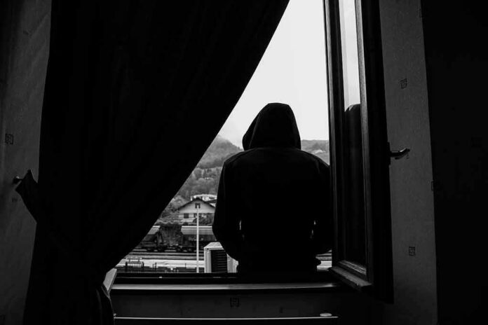 shutterstock_2066137799 hooded figure sitting on a windowsill looking outside