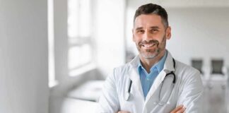 Smiling male doctor with stethoscope crossing arms in bright clinic