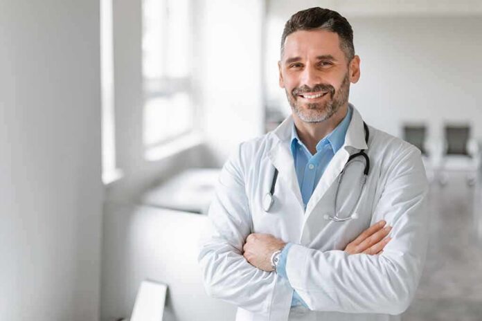 shutterstock_2281024719 Smiling male doctor with stethoscope crossing arms in bright clinic