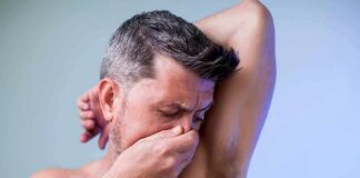 Man covering his nose while smelling his armpit