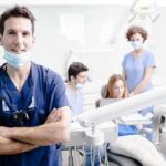 Fake Reviews CRACKDOWN Slams Dentists Dentist in scrubs stands with arms crossed in a bright dental clinic