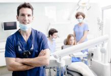 Dentist in scrubs stands with arms crossed in a bright dental clinic