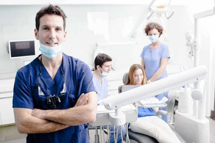 shutterstock_138700625 Dentist in scrubs stands with arms crossed in a bright dental clinic