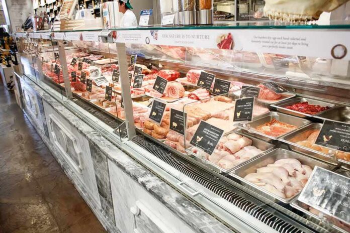 shutterstock_1672191394 butcher counter with assorted meats in trays behind glass
