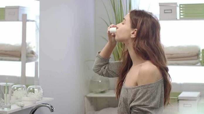 woman in bathroom using nasal spray