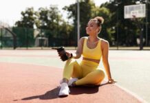 Woman in yellow activewear sitting on outdoor court with water bottle