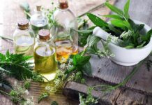 Glass bottles of herbal oils beside a mortar and pestle with fresh green herbs