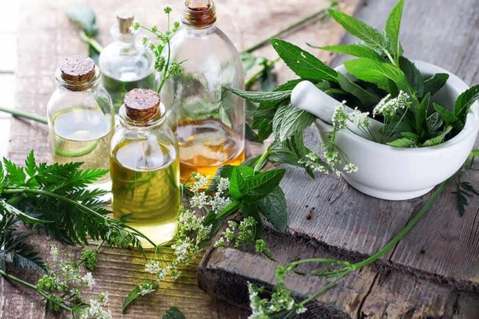 Glass bottles of herbal oils beside a mortar and pestle with fresh green herbs