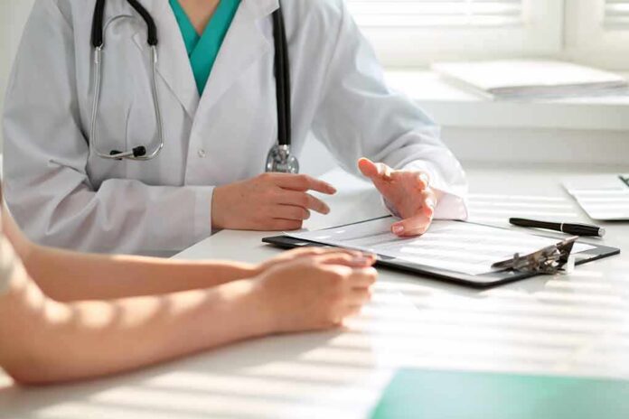 shutterstock_500753095 Doctor discusses medical notes with patient at a desk