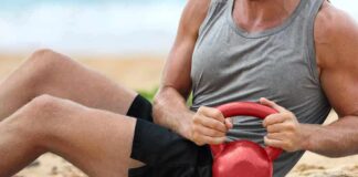 Man doing sit-ups with a red kettlebell on a beach mat